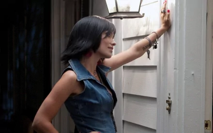HD PC desktop wallpaper featuring celebrity Olivia Wilde in a side profile, wearing a sleeveless denim top and standing by a door with a lantern overhead.
