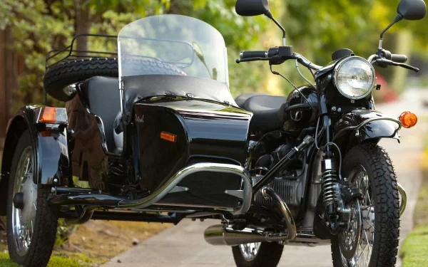 HD wallpaper of a black Russian Ural motorcycle with a sidecar, parked on a road with green foliage in the background.
