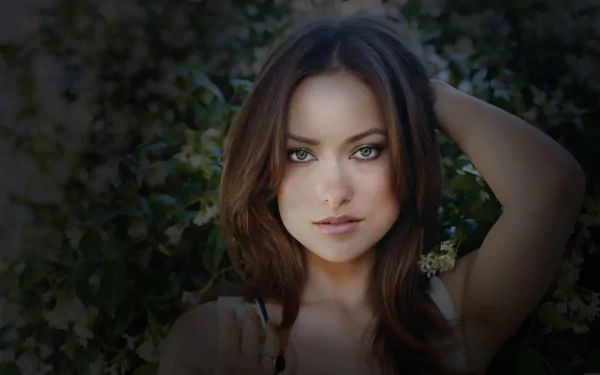 A stunning HD desktop wallpaper featuring Olivia Wilde, captured amidst lush greenery with captivating eyes and a confident expression.