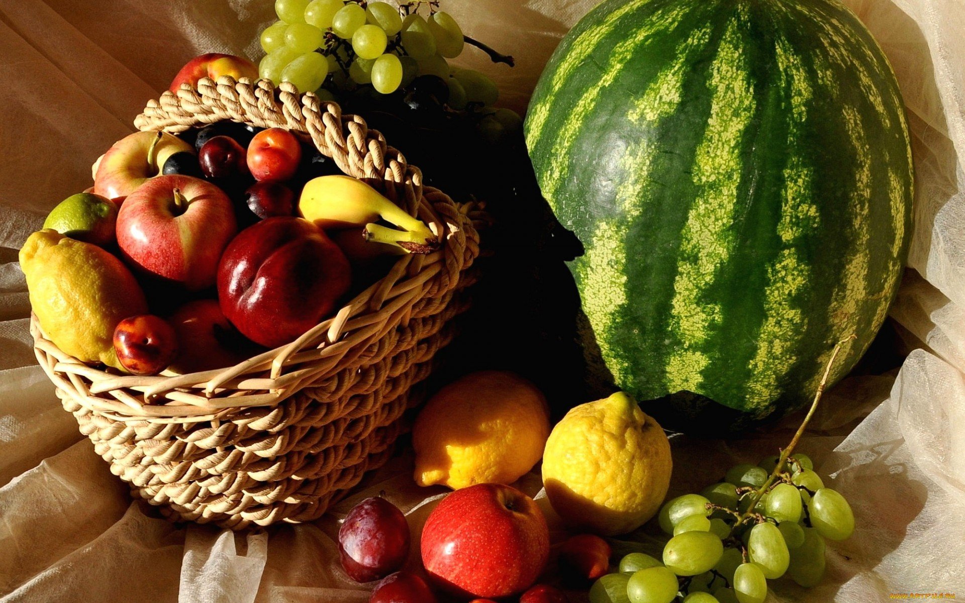 HD PC desktop wallpaper featuring a vibrant arrangement of fresh fruits, including a watermelon, grapes, apples, pears, and lemons in a woven basket.