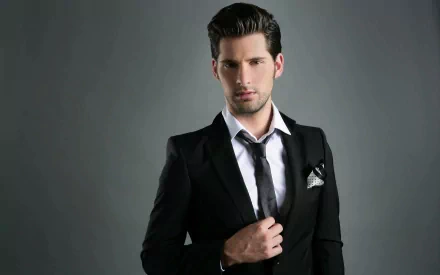 Handsome man in a black suit with a loosened tie poses against a plain gray background, featured as an HD PC desktop wallpaper and background.