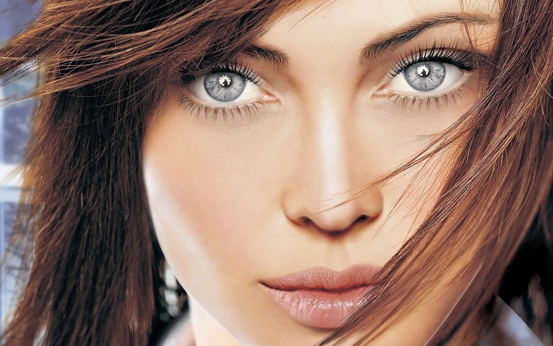 Close-up HD desktop wallpaper of a woman model with striking light gray eyes and flowing brown hair.