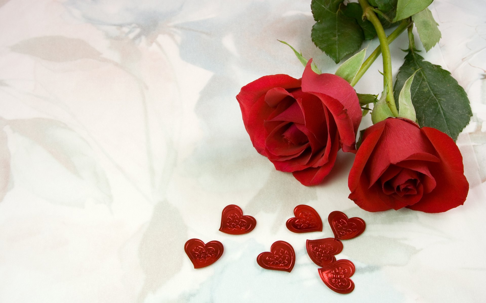 HD photography desktop wallpaper featuring two red roses and scattered red heart-shaped decorations, symbolizing love and romance on a soft white background.