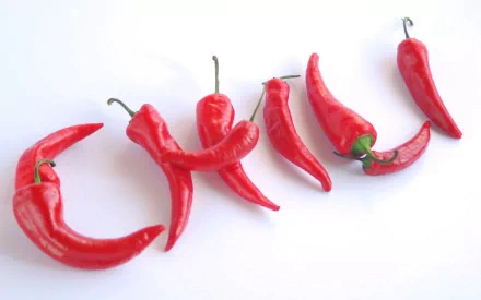HD desktop wallpaper featuring a close-up of several red chili peppers arranged on a white background, highlighting their vibrant color and texture.