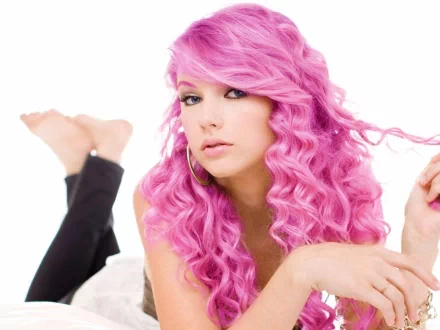 A vibrant HD wallpaper featuring a musician with striking pink curly hair, showcasing her artistic flair and charisma, set against a clean white background.