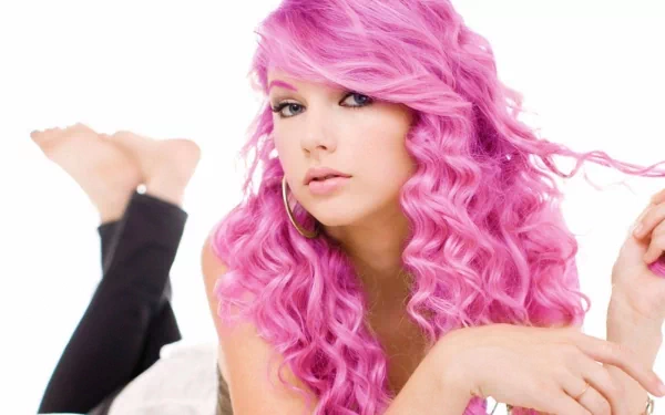 A vibrant HD wallpaper featuring a musician with striking pink curly hair, showcasing her artistic flair and charisma, set against a clean white background.