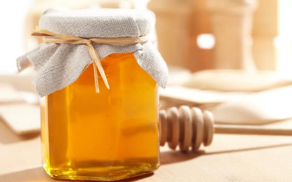 HD desktop wallpaper showing a jar of honey with a cloth cover and a wooden honey dipper on a softly lit surface.