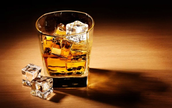 A close-up of a glass of whisky on a wooden surface, filled with ice cubes, creating a warm and inviting atmosphere. This HD desktop wallpaper captures the essence of relaxation.