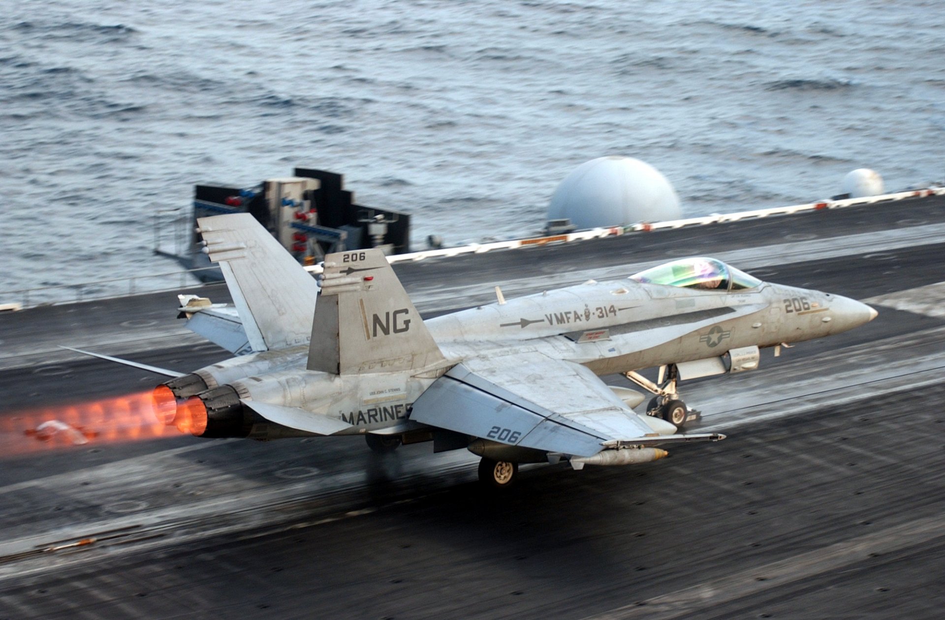 HD desktop wallpaper showing a McDonnell Douglas F/A-18 Hornet military jet launching from an aircraft carrier deck over the ocean.