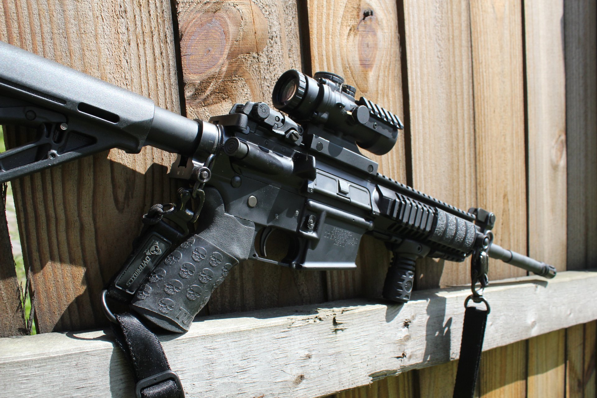 5K Ultra HD PC desktop wallpaper of a man-made assault rifle resting on a wooden fence, close-up showing stock, rail, optic and barrel.