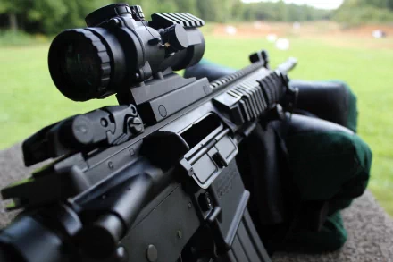 Close-up of a black assault rifle with a scope, set against an outdoor backdrop, designed as a 4K Ultra HD PC desktop wallpaper and background.
