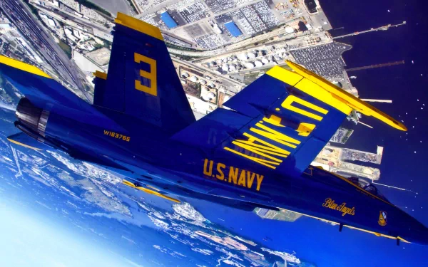 A blue U.S. Navy McDonnell Douglas F/A-18 Hornet from the Blue Angels performs a military air show maneuver over a coastal city in this HD desktop wallpaper.