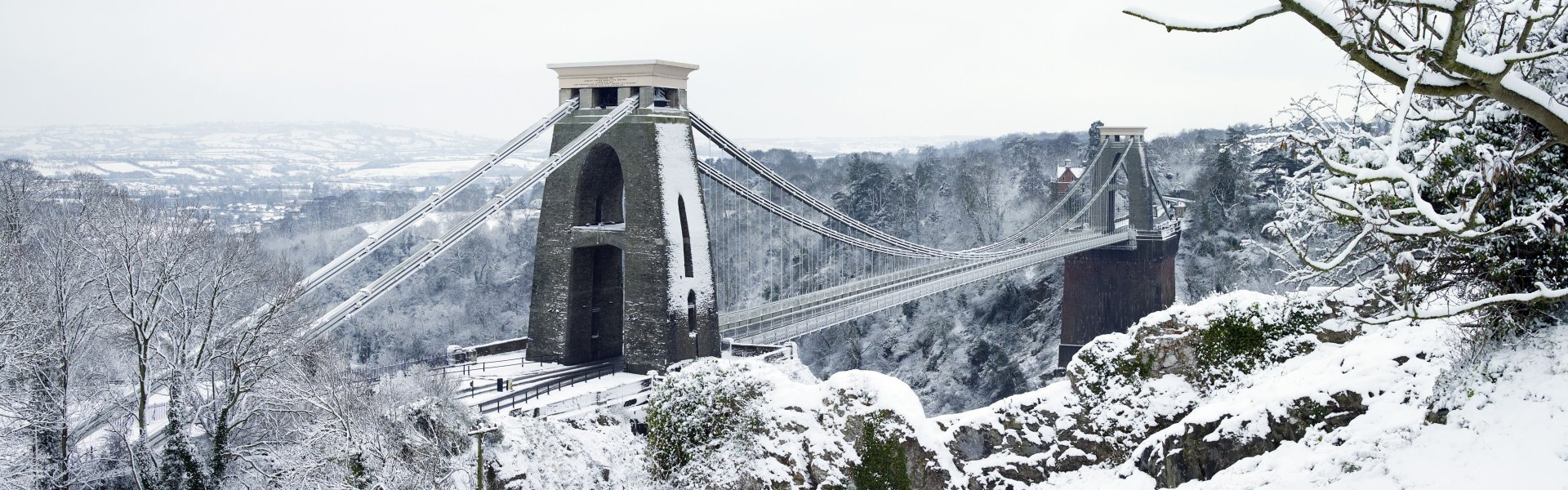Snow-dusted Clifton Suspension Bridge spanning the frosted Avon Gorge near Bristol — HD desktop wallpaper of the man-made landmark.