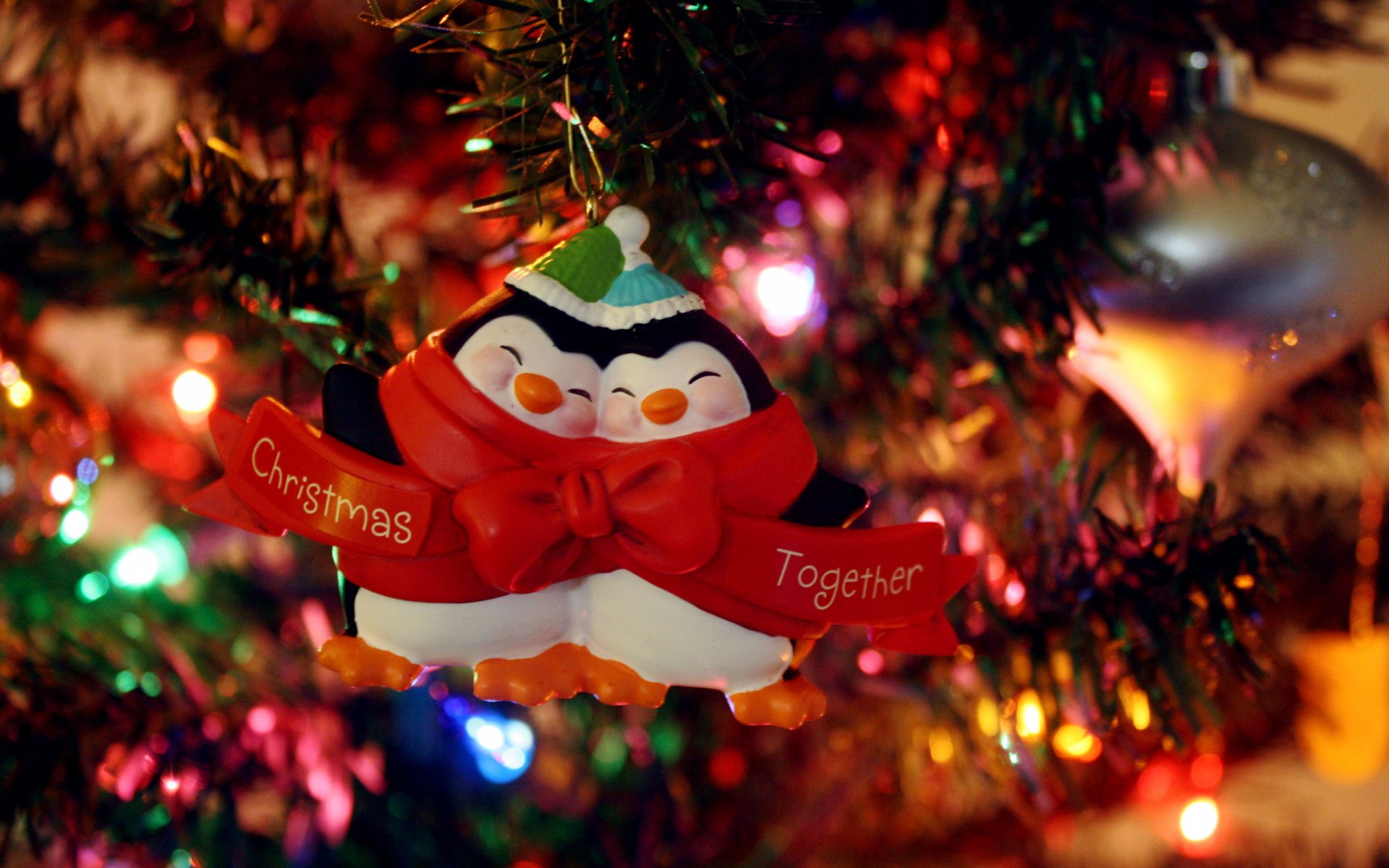 A festive penguin ornament with a red scarf and the words Christmas Together hangs on a decorated tree, surrounded by colorful holiday lights, creating a cheerful Christmas atmosphere.
