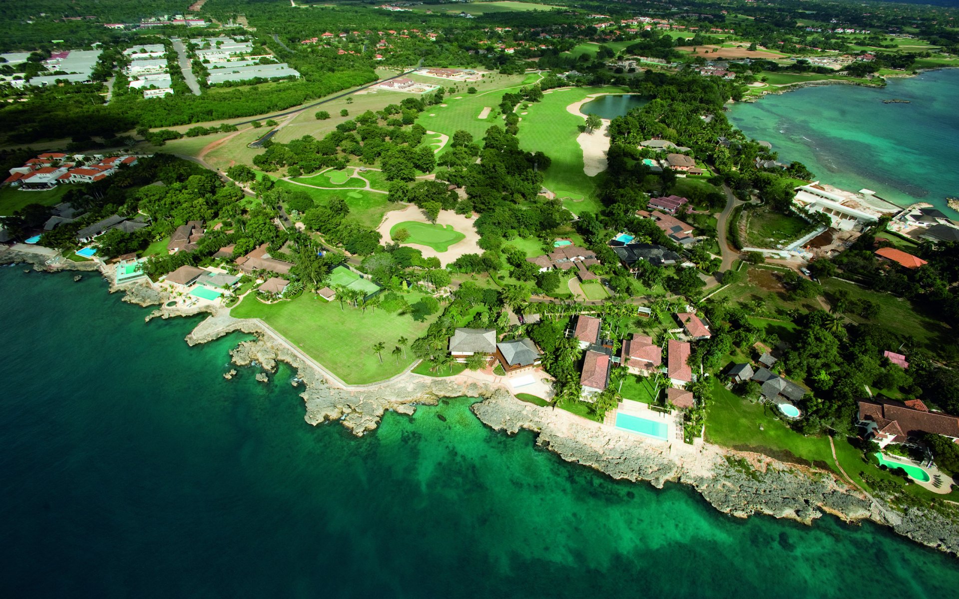 Aerial view of a lush coastal landscape featuring vibrant greenery, a golf course, and serene blue waters, capturing the beauty of nature as a stunning HD desktop wallpaper.