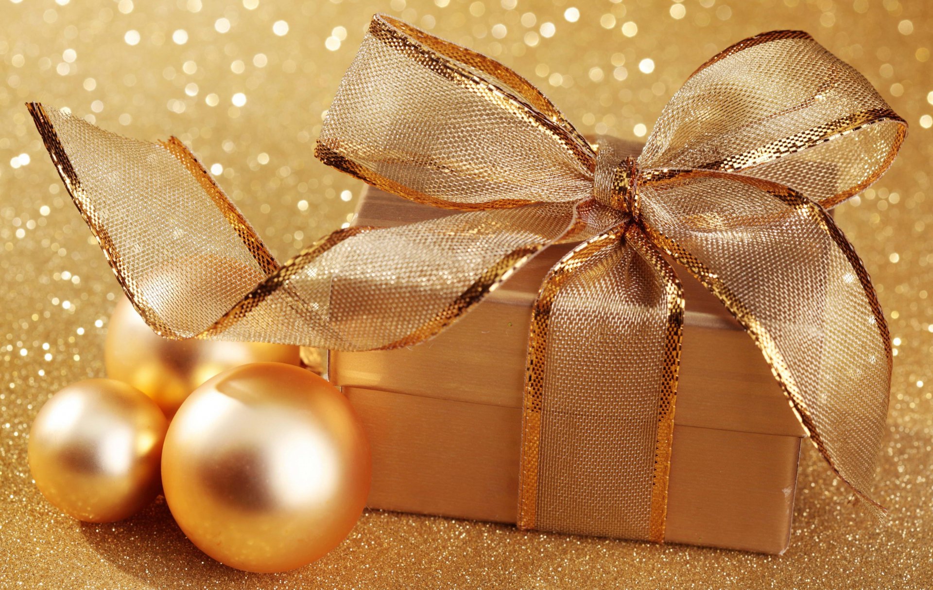 A golden gift box with a shimmering ribbon and matching Christmas ornaments set against a sparkling gold background, captured in 4K Ultra HD as a festive holiday desktop wallpaper.