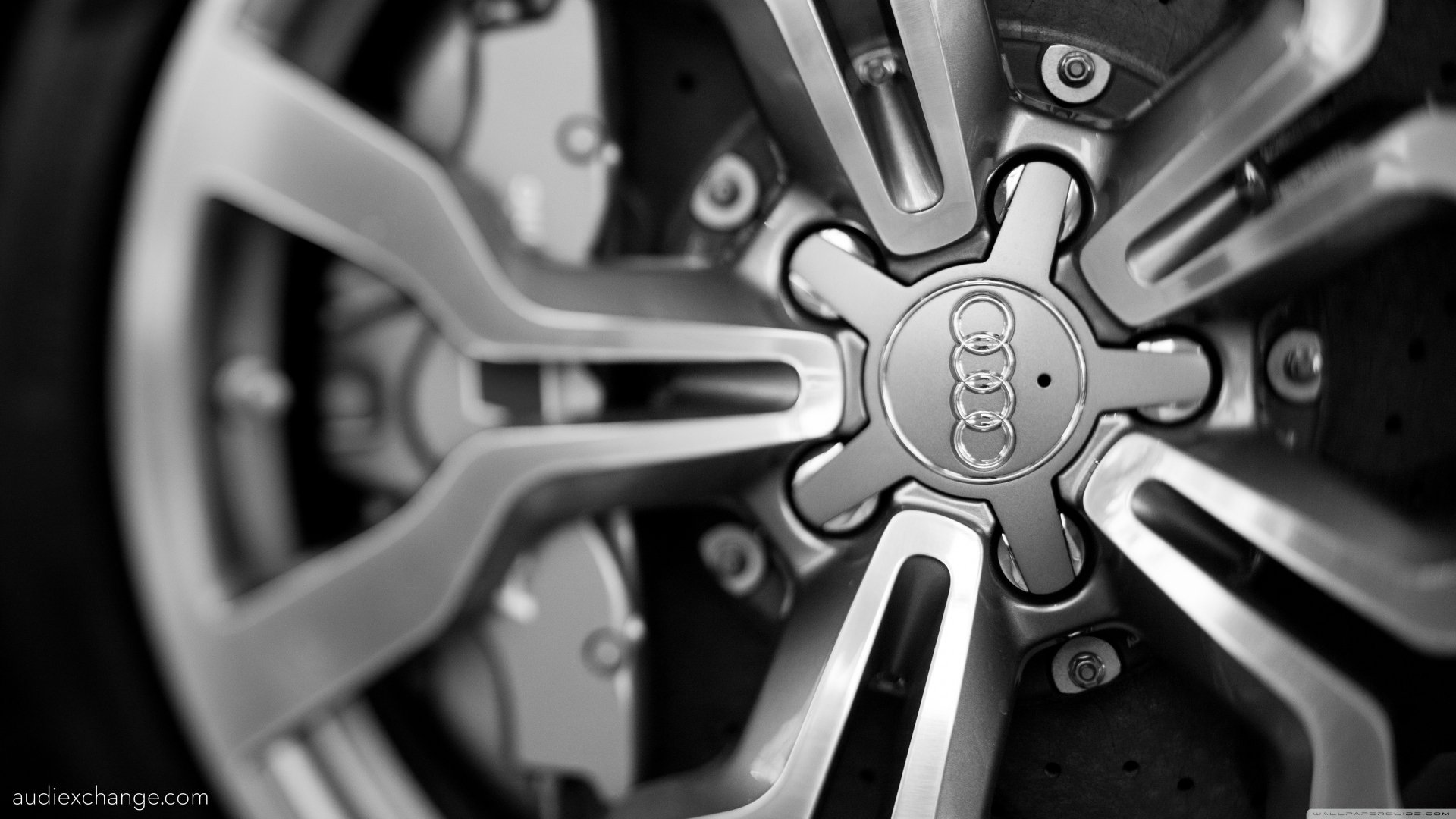 Black-and-white 4K Ultra HD PC desktop wallpaper of a close-up Audi vehicle alloy wheel hub and spokes, focused on the central Audi logo.