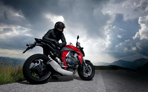A Honda CBR motorcycle parked on the roadside, with a rider in black gear, set against a dramatic sky and rolling hills, creating a striking HD desktop wallpaper.