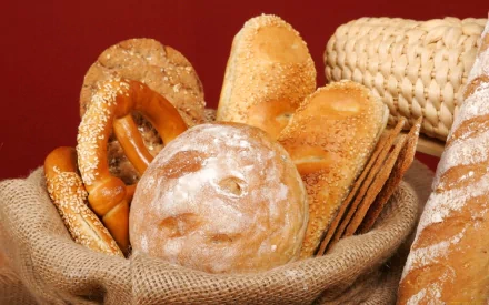 HD PC desktop wallpaper featuring an assortment of fresh bread and pretzels in a rustic burlap sack against a warm red background.