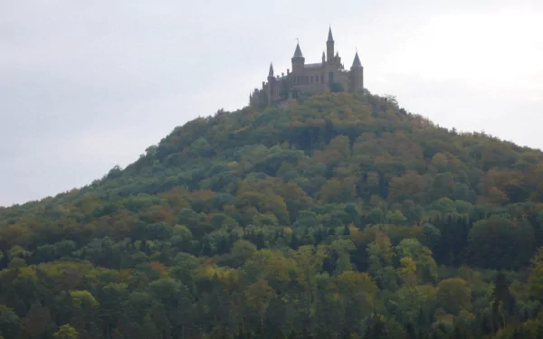 HD desktop wallpaper featuring the man-made Hohenzollern Castle perched atop a forested hill under a cloudy sky.