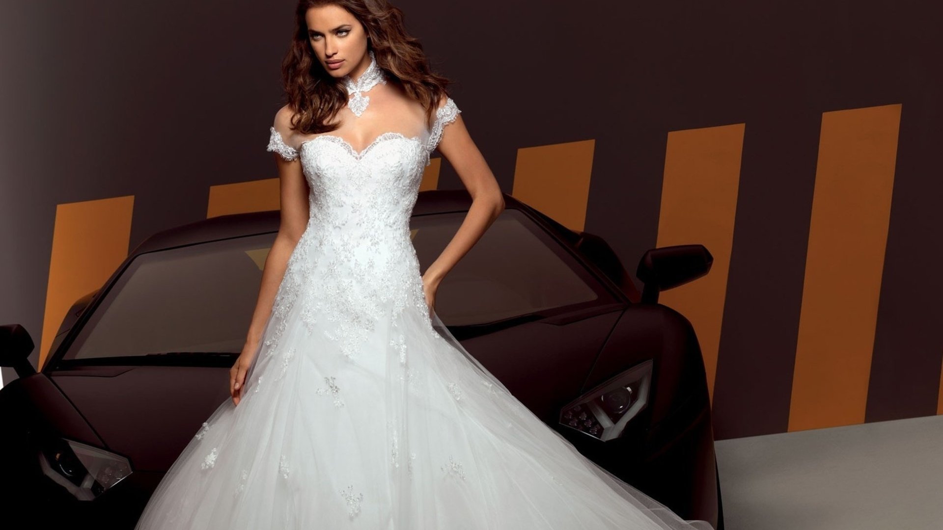 HD PC desktop wallpaper featuring celebrity Irina Shayk in an elegant white gown standing in front of a black sports car with a striped background.