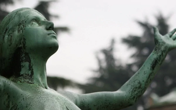 4K Ultra HD PC desktop wallpaper: green-patinated man-made statue of a figure with arms outstretched, gazing skyward against a soft-focus backdrop of trees.