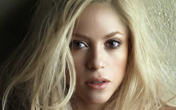 HD PC desktop wallpaper featuring a close-up portrait of Shakira with natural makeup and loose blonde hair, highlighting her expressive eyes.