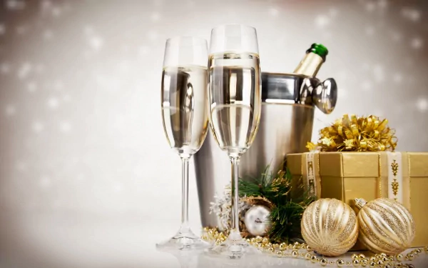 Holiday New Year 5K Ultra HD PC desktop wallpaper: two champagne flutes, an ice bucket with a bottle, gold gift box and ornaments against a soft bokeh background.