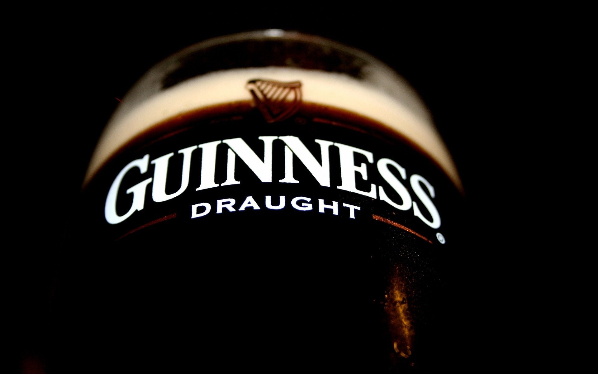 A close-up of a glass of Guinness Draught against a dark background, showcasing its rich color and creamy head, designed as an HD desktop wallpaper.