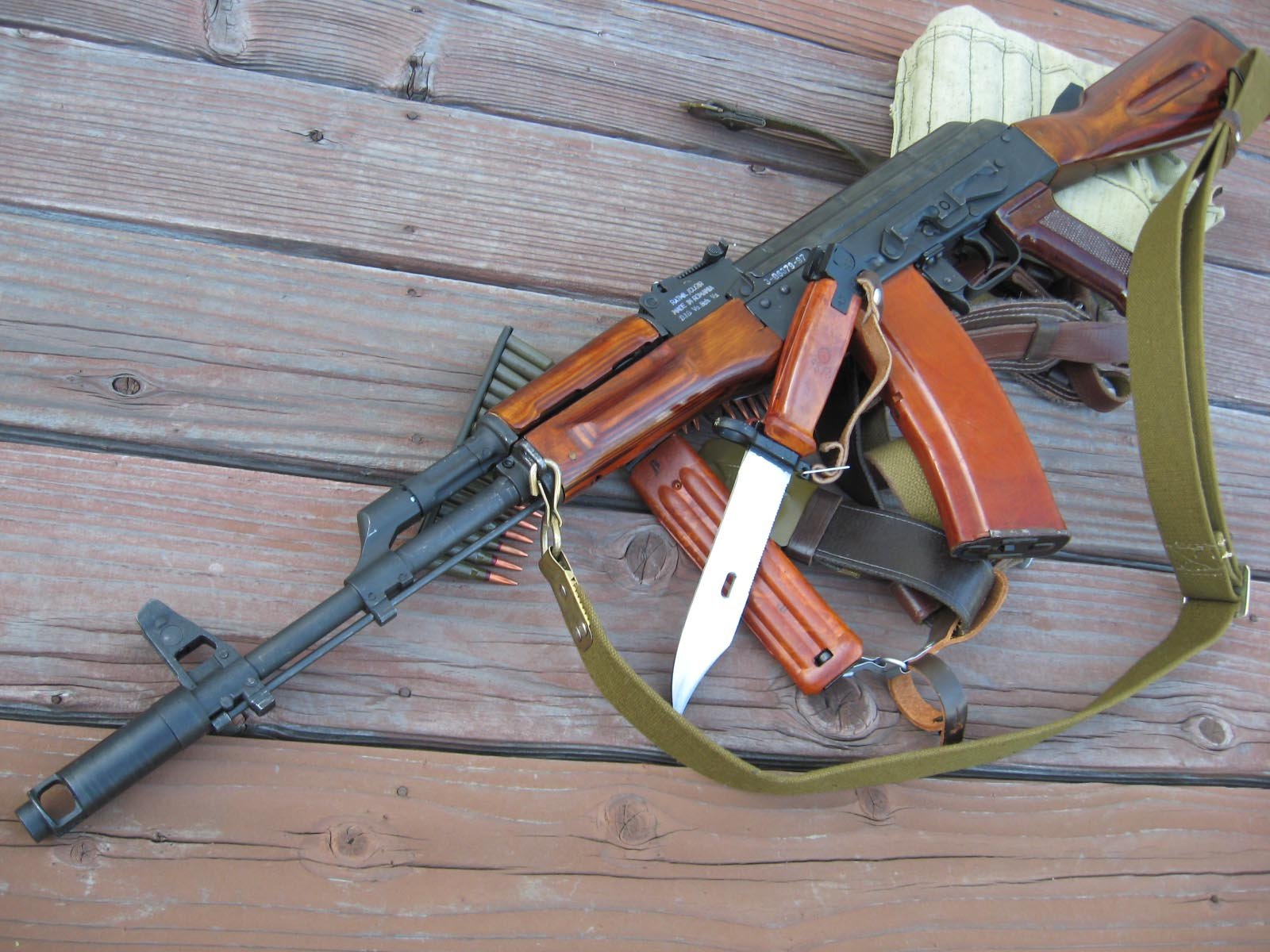 HD desktop wallpaper featuring a man-made AKM assault rifle with a bayonet attached, resting on wooden planks.