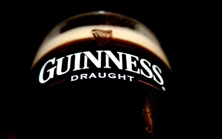 A close-up of a glass of Guinness Draught against a dark background, showcasing its rich color and creamy head, designed as an HD desktop wallpaper.