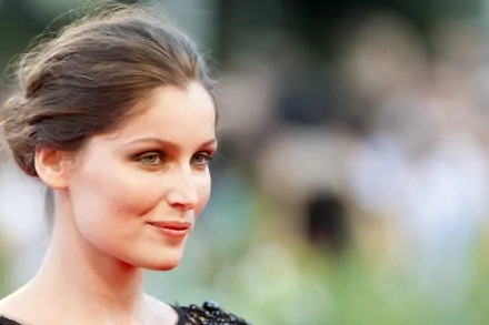 Close-up portrait of a poised woman with swept-back hair and subtle makeup, blurred crowd background — 2K Quad HD PC desktop wallpaper.