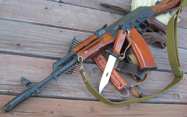 HD desktop wallpaper featuring a man-made AKM assault rifle with a bayonet attached, resting on wooden planks.