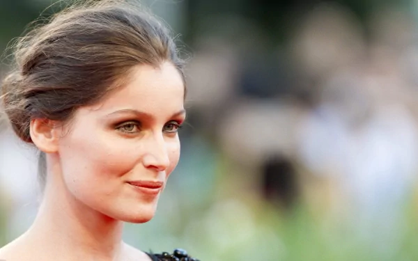 Close-up portrait of a poised woman with swept-back hair and subtle makeup, blurred crowd background — 2K Quad HD PC desktop wallpaper.