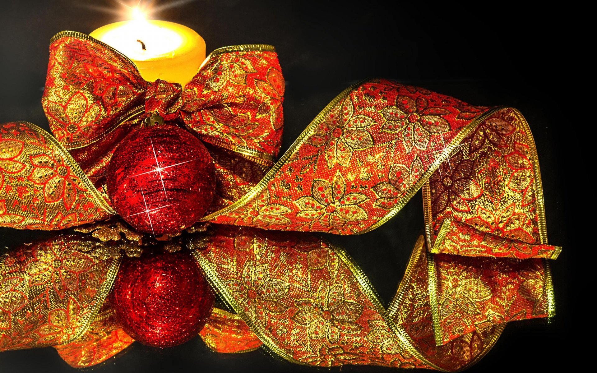 A glowing candle surrounded by a red Christmas ornament and ornate gold-red ribbon, creating a festive holiday scene for an HD PC desktop wallpaper.