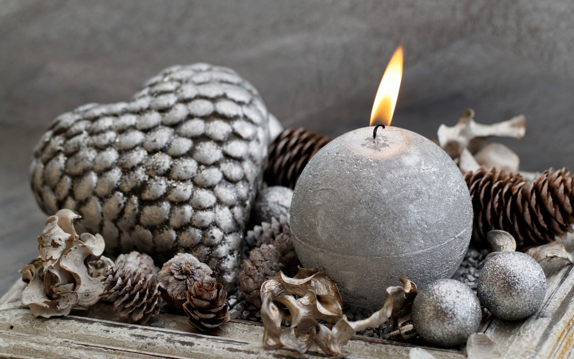 HD photography wallpaper featuring a lit round candle surrounded by silver pine cones and heart-shaped decor on a textured surface.