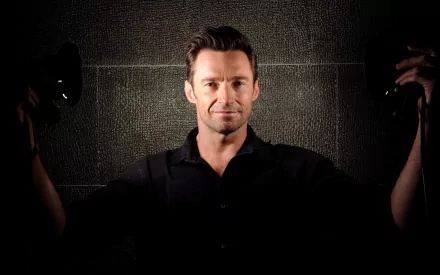 Hugh Jackman poses confidently in a stylish dark setting, making this HD wallpaper a striking addition to any desktop background.