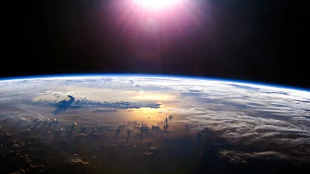 HD desktop wallpaper showing Earth from space with sunlight casting reflections over clouds, capturing the beauty of nature from a high orbit perspective.