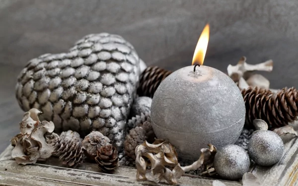 HD photography wallpaper featuring a lit round candle surrounded by silver pine cones and heart-shaped decor on a textured surface.