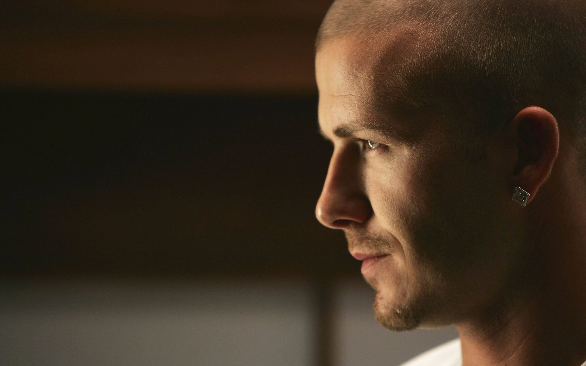 Close-up profile of a male athlete with shaved head and earring, warm low-key lighting; sports-themed 2K Quad HD PC desktop wallpaper/background.
