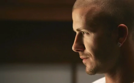 Close-up profile of a male athlete with shaved head and earring, warm low-key lighting; sports-themed 2K Quad HD PC desktop wallpaper/background.