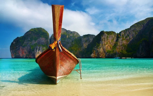 A vibrant HD desktop wallpaper of a traditional canoe on a sandy beach, turquoise ocean, and lush coastline in Thailand showcasing nature and earth’s beauty.
