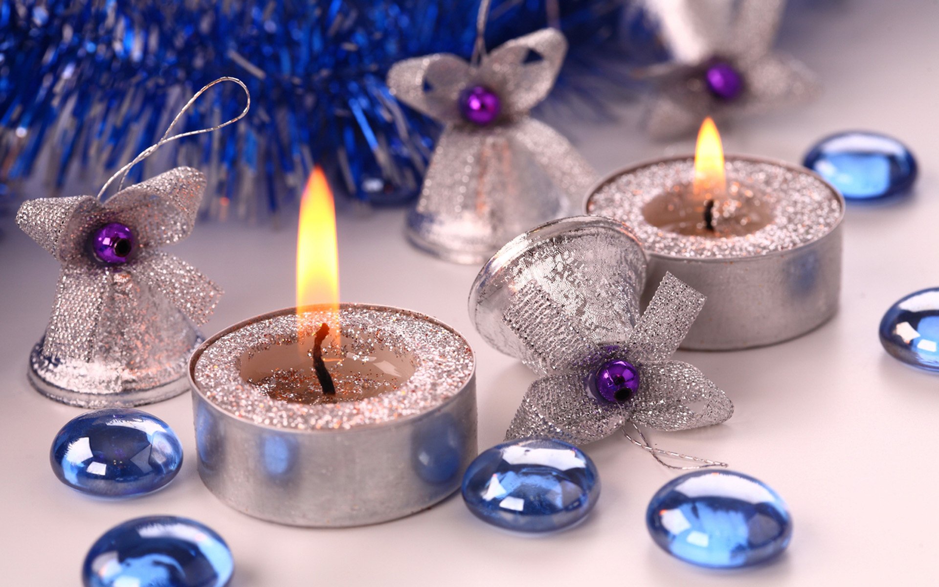 A festive arrangement of silver Christmas ornaments and candles, featuring delicate bows and blue decorations, creates a warm holiday atmosphere in this HD desktop wallpaper.