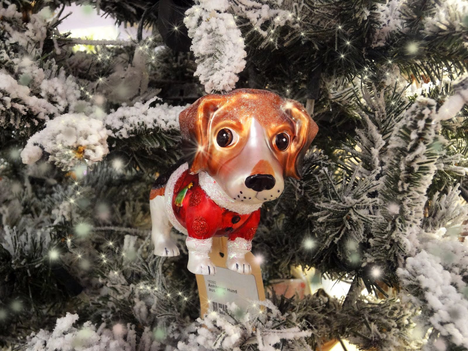 A charming dog-shaped ornament wearing a red scarf hangs on a snow-dusted Christmas tree, enhancing the festive spirit of the holiday season. This HD wallpaper captures the joy of Christmas.