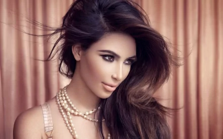 HD wallpaper featuring Kim Kardashian, showcasing her elegant hairstyle and pearl necklace against a soft, warm-toned backdrop.