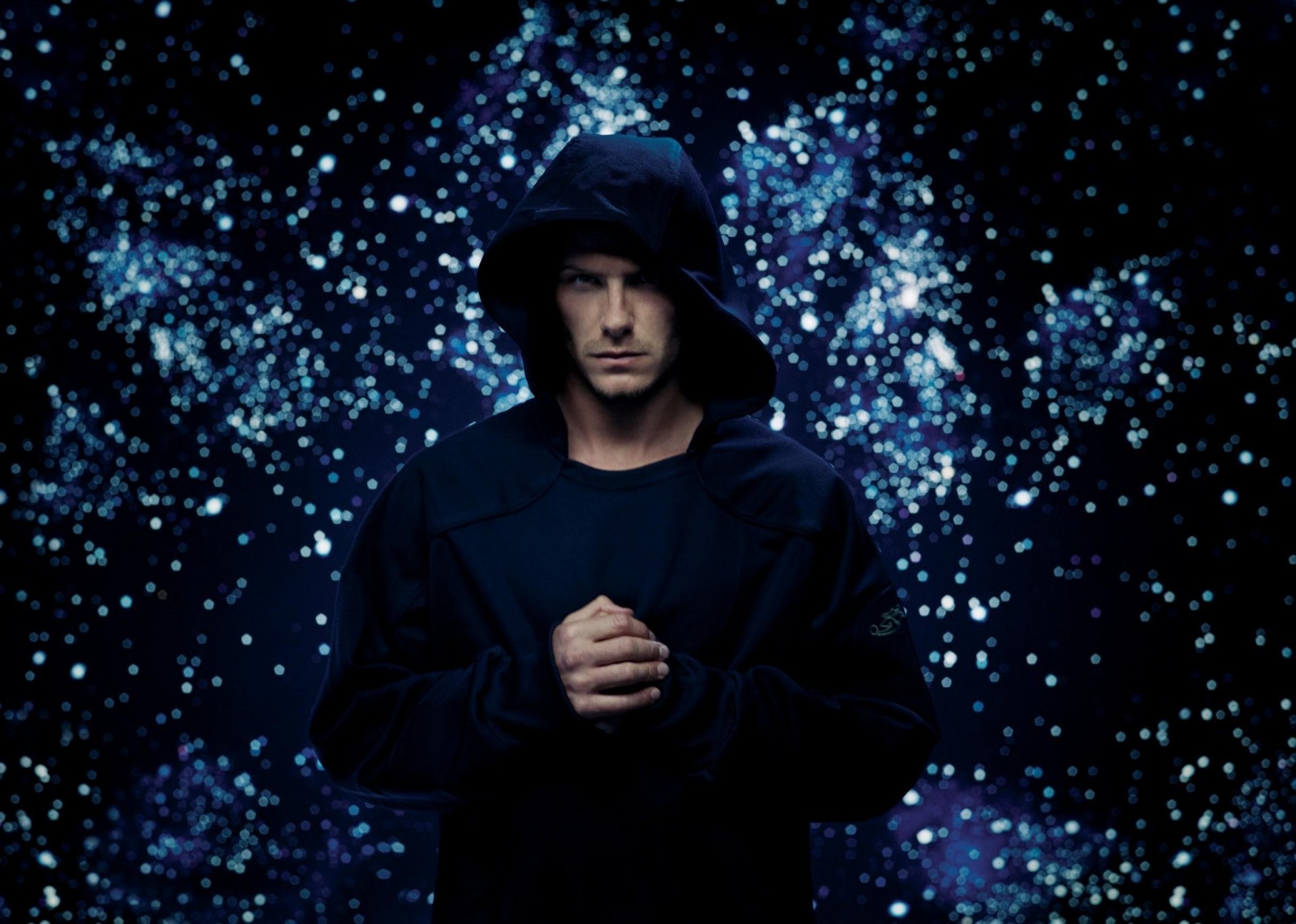 HD PC desktop wallpaper of David Beckham in a dark hooded jacket, set against a sparkling, starry background, capturing a moody sports-themed atmosphere.