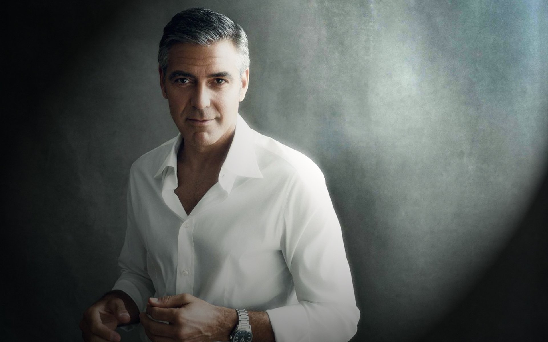 HD PC desktop wallpaper of a male celebrity in a white shirt against a soft gray textured backdrop, posed relaxed and confident with cinematic, moody lighting.