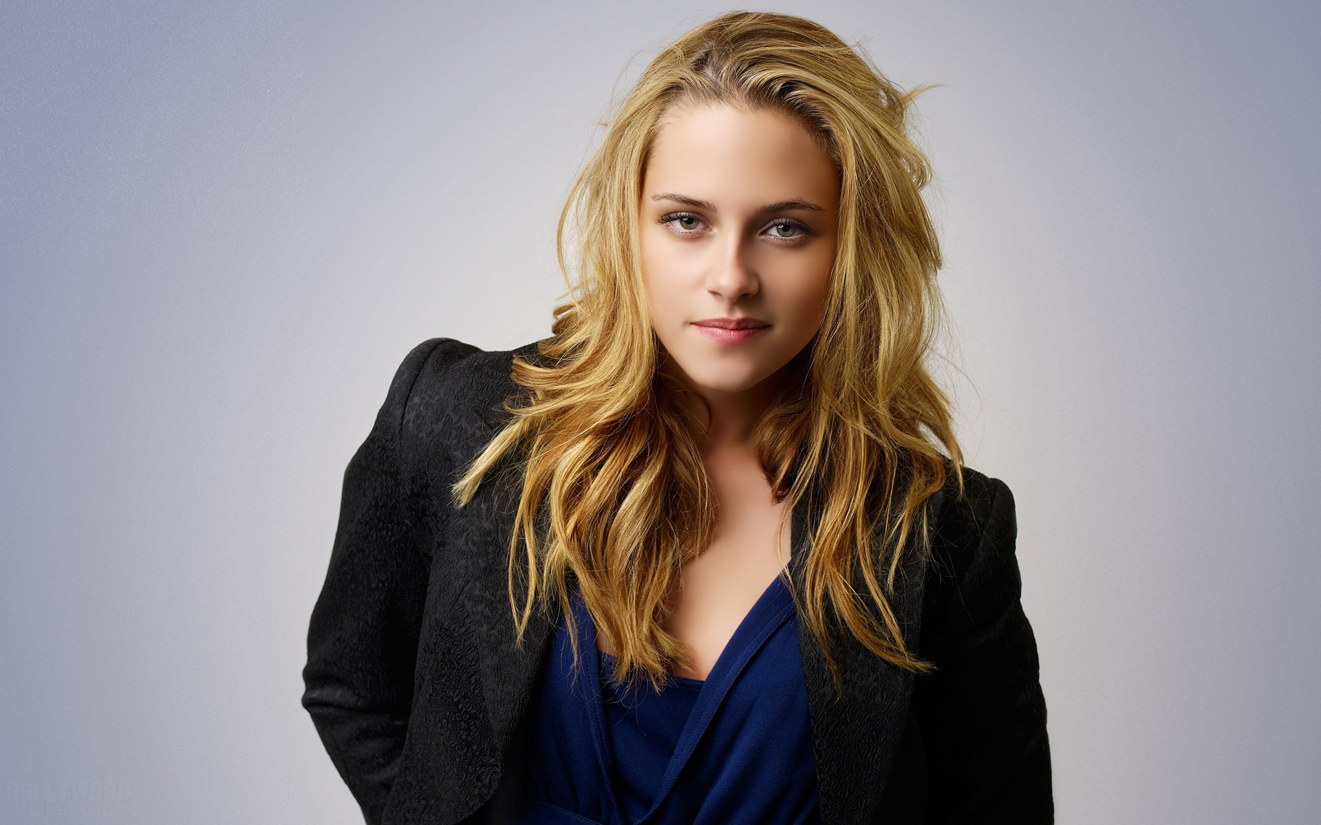 HD desktop wallpaper featuring celebrity Kristen Stewart, wearing a dark blazer over a blue top, posing confidently with a neutral background.
