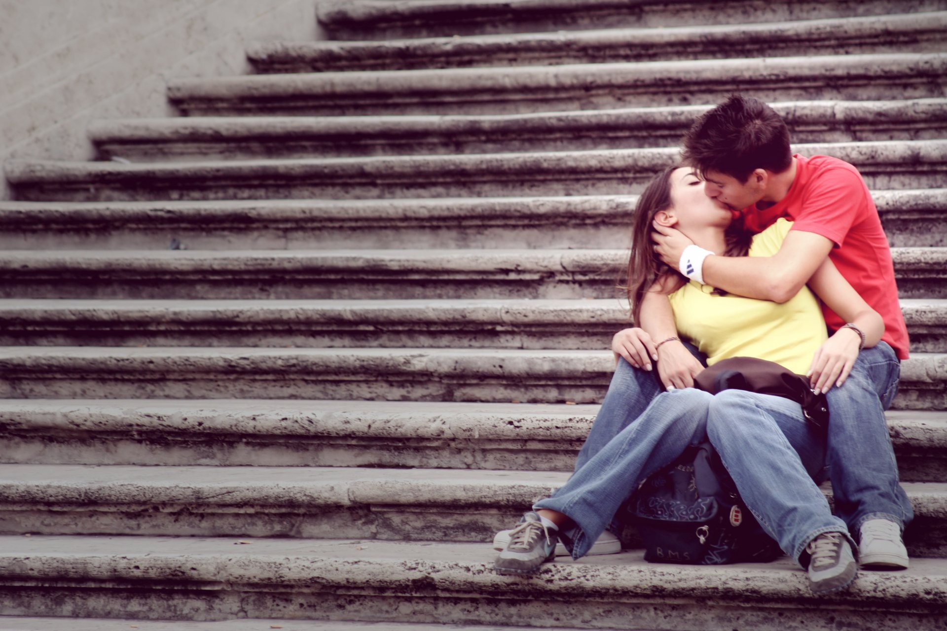 HD photography desktop wallpaper capturing a couple sharing a tender kiss while sitting on stone steps, embodying a moment of love and connection.