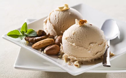 Delicious ice cream scoops served on a white plate, garnished with nuts and mint, creating an enticing food display for a high-definition desktop wallpaper.